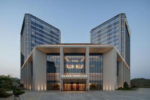 a large glass building with two tall buildings at Grand Mercure Hangzhou Qingshan Lake in Hangzhou