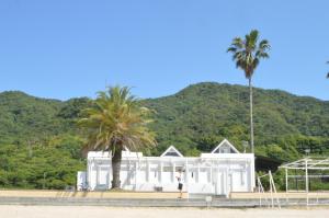 un homme debout devant une maison blanche avec un palmier dans l'établissement アグリート島時間, à Onomichi