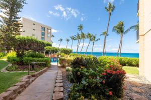 a walkway through a garden with palm trees and the ocean at Kealia Resort 601 in Kihei