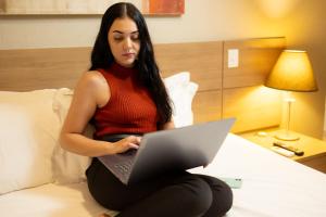 una mujer sentada en una cama usando un portátil en Ville Hotel Gramadão, en Votuporanga