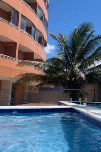 a swimming pool in front of a building with a palm tree at Loft Temporada Praia do Meio in Natal