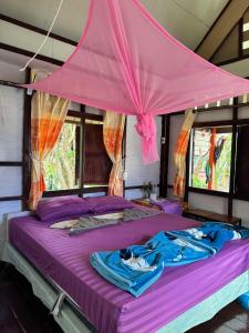 a bed with purple sheets and a pink canopy at Baan Suan Kayoo 2 Buffalo Bay Aow Khao Kwai in Ko Phayam