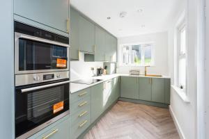 a large kitchen with green cabinets and appliances at Luxurious 10-Person Modern House with Garden in Central Tonbridge in Kent