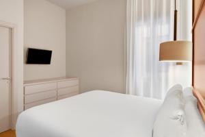 a white bedroom with a bed and a television at B&B HOTEL Apartamentos Madrid Centro Fuencarral 46 in Madrid