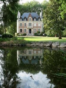 duży dom z odbiciem w zbiorniku wody w obiekcie Maison d'hôtes Le Manoir de Contres w mieście Contres