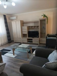 Una sala de estar con televisión y una mesa de centro de cristal. en Aqua-Vital Prémium Apartmanok, en Hajdúszoboszló