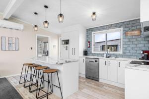 a kitchen with white cabinets and bar stools at Sea you on Leo in Waihi Beach