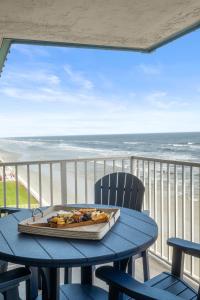 a table with a tray of food on a balcony with the ocean at Serenity Shores Renovated Top Floor Condo w Stunning Ocean Views in New Smyrna Beach
