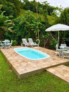 einen Pool mit Stühlen, Tischen und einem Sonnenschirm in der Unterkunft Casa no Sitio em São José do Barreiro in São José do Barreiro