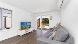 a living room with a gray couch and a window at 'Coastal Harmony Cottage' by HolidayCo in Hardys Bay