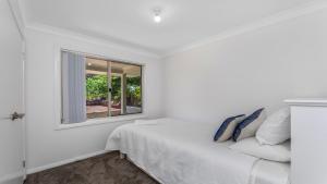 a white bedroom with a white bed and a window at 'Coastal Harmony Cottage' by HolidayCo in Hardys Bay