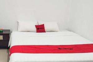a white bed with a red pillow on it at RedDoorz Syariah at Sayang Ibu Village Nongsa Batam in Nongsa