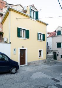 a yellow house with green shutters and a car parked in front at La Perla Luxury Apartments in Split