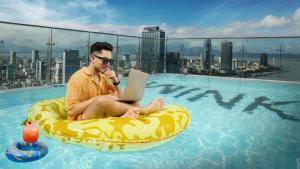 um homem sentado num anel insuflável numa piscina com um portátil em Wink Icon Hotel Danang Riverside - Luxury Suites - 24hrs Stay & Rooftop Pool Bar em Da Nang