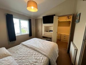 a bedroom with a bed and a window and a television at Stunning Lodge Boasting Large Decking Area At California Cliffs Ref 50008L in Great Yarmouth