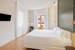 a white bedroom with a large bed and a television at B&B HOTEL Apartamentos Madrid Centro Fuencarral 46 in Madrid