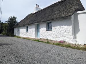 a white cottage with a thatched roof on a road at Goggin Cottage in New Kildimo