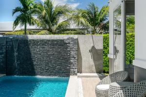 a swimming pool with two chairs next to a brick wall at Friendly Kamala Garden View in Kamala Beach