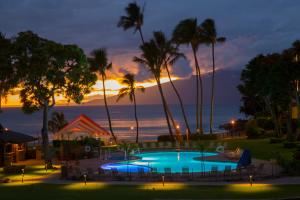 een zwembad met palmbomen en een zonsondergang op de achtergrond bij Napili Kai Beach Resort in Lahaina