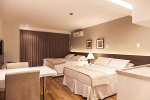 a hotel room with two beds and a table at Hotel Atmosfera Feira de Santana in Feira de Santana