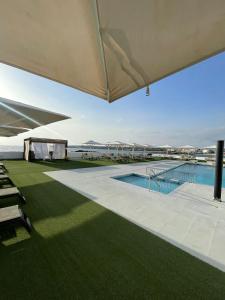 a pool with a large umbrella and green grass at Hotel Roca Bella in Es Pujols