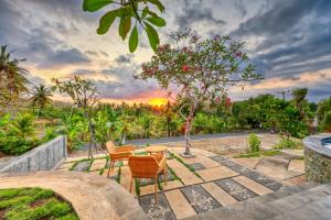a patio with chairs and a table with a sunset in the background at NG Sweet Home in Nusa Penida