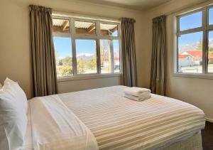 a bedroom with a white bed with two windows at Matagouri Cottage - Lake Tekapo in Lake Tekapo +7 photos