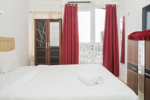 a bedroom with a white bed with red curtains and a window at Fully Furnished with Cozy Design Studio Poris 88 Apartment By Travelio in Tangerang