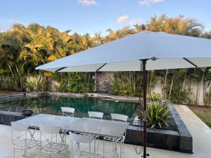 a table and chairs under an umbrella next to a swimming pool at Blue Palm Villa with Private Pool & Tropical Garden in Cap Malheureux