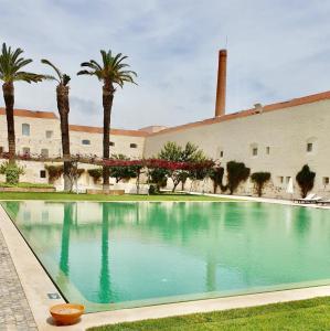 a swimming pool in front of a building with palm trees at Apartamento Convento das Bernadas Tavira in Tavira