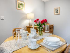 un tavolo con piatti e bicchieri e un vaso di rose di Coed Y Gaer Annexe - Uk43776 a Llansilin
