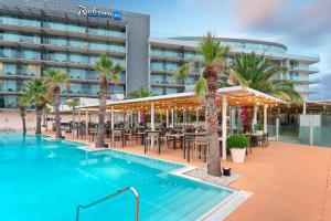 an outdoor pool with tables and chairs and palm trees at Radisson Blu Resort & Spa in Split