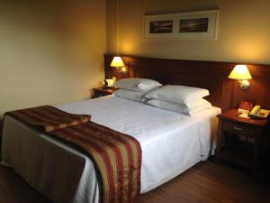 a hotel room with a bed with white sheets and pillows at Flat Gramado Alpen in Gramado