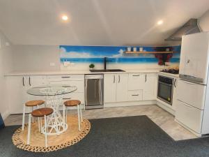 a kitchen with white cabinets and a table and stools at Welcome to Howick Auckland in Auckland +6 photos