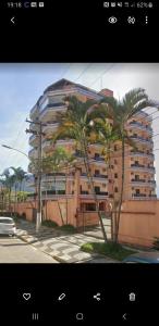 a large building with palm trees in front of it at Apartamento a 50 metros da praia in Caraguatatuba