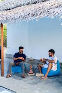 two men sitting on a blue couch under a straw umbrella at Bedrock Beach Villas in Kalpitiya