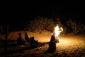 a group of people sitting around a fire in the sand at Bedrock Beach Villas in Kalpitiya