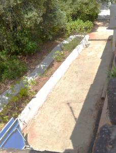 a sidewalk with a white curb next to some bushes at Le Patio Bleu in La Crau