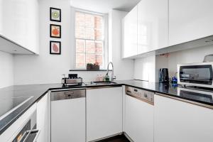 a white kitchen with white cabinets and a microwave at The Bronwen in London