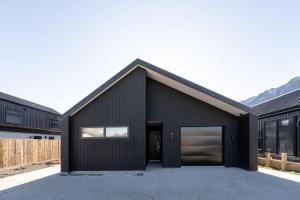 a black house with a garage and mountains in the background at Amazing Retreat in Queenstown in Frankton Wharf