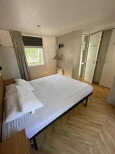 a bedroom with a large bed with white sheets and a window at Mobil Home Les Viviers Cap Ferret in Lège-Cap-Ferret