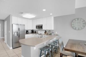 a kitchen with white cabinets and a table and a refrigerator at Lighthouse 1408 by Liquid Life in Gulf Shores