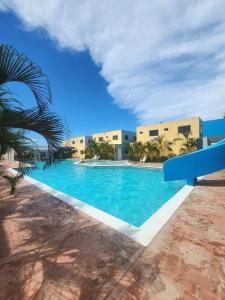 a blue swimming pool with a palm tree and buildings at Apartamento soñado de Playa in El Marite