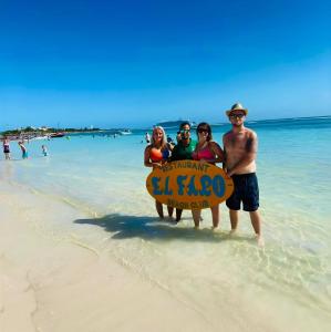 a group of people standing on a beach with a sign at Day Pass Todo Incluido El Faro Beach Club & Restaurant Solo Experiencia no incluye alojamiento - 85 USD por persona in Mahahual