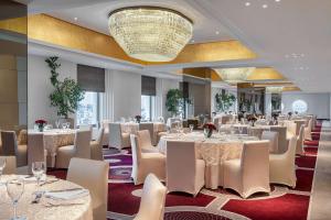 ジッダにあるThe Hotel Galleria Jeddah, Curio Collection by Hiltonの白いテーブルと椅子、シャンデリアのあるレストラン