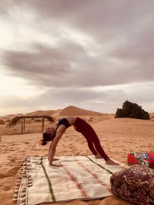 a woman doing yoga on a blanket in the desert at Eco Merzouga luxury camp in Merzouga