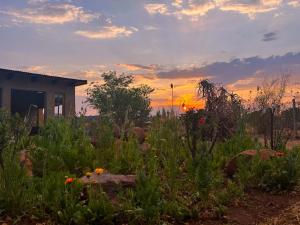 un jardin avec une maison et des fleurs devant un coucher de soleil dans l'établissement Lekker Plekkie Farm Cottage, à Hekpoort