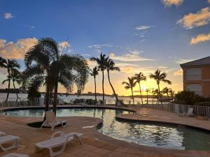 - une piscine avec des chaises et des palmiers au coucher du soleil dans l'établissement appartement au bord de l'eau sxm, à Baie Nettlé