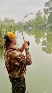 a man holding a fishing rod on a lake at Füzesem Apartman in Békésszentandrás