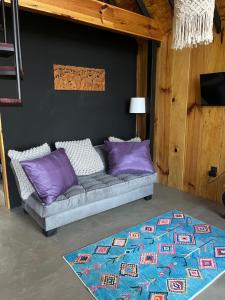 a couch with purple pillows in a room with a rug at Mi Refugio Nordico Buho Cabin in San Miguel